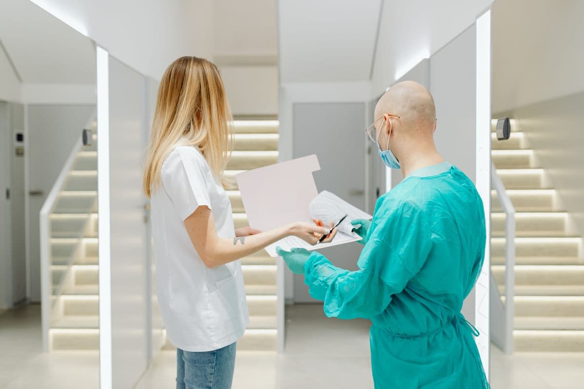 Senior clinical supervisor reviewing patient records and care plans with a clinician on a tablet in a modern hospital wing.